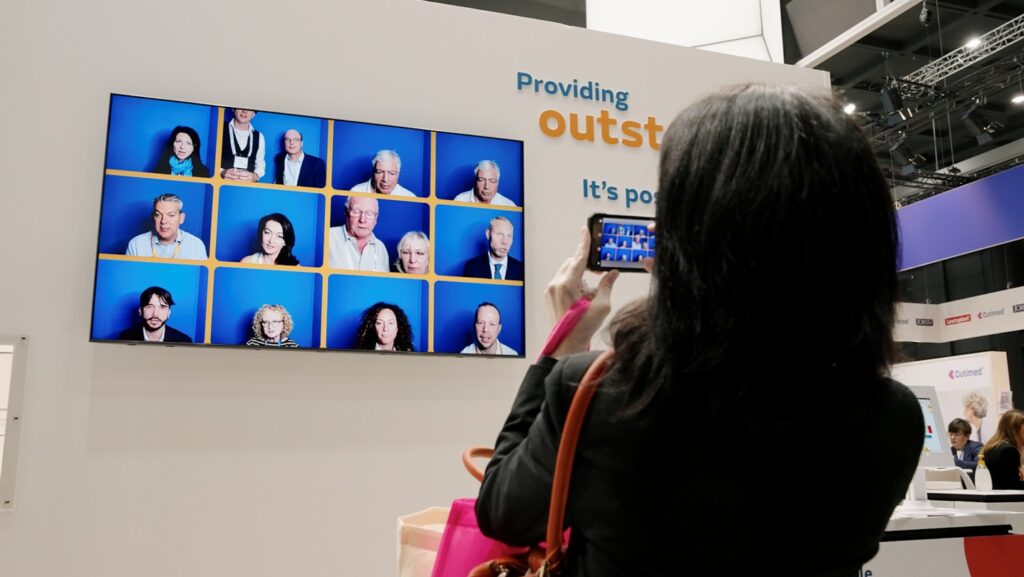 Woman capturing a selfie on a large interactive screen at a clinical conference, part of a delegate engagement video booth for Smith+Nephew’s clinical event marketing campaign at EWMA by EatMoreFruit Communications healthcare pr agency