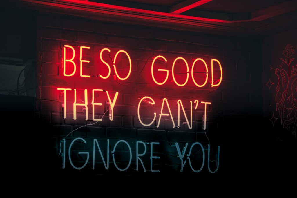 Red neon text on a black background that reads "Be So Good They Can