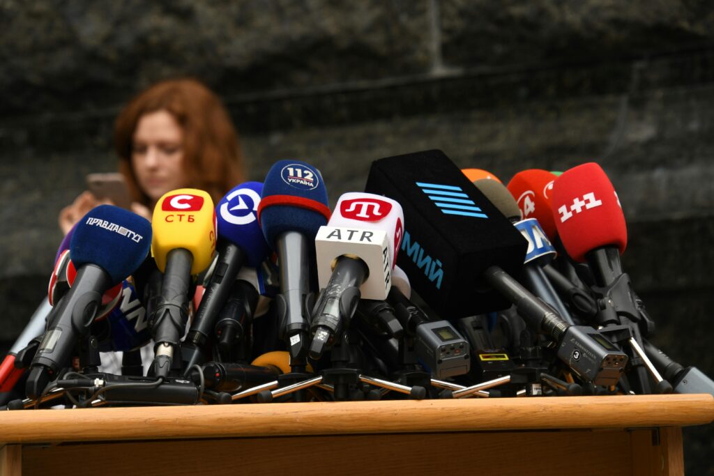 woman standing in front of several media microphones in press conference style